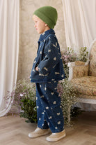 Child wearing a denim outfit with bird patterns in a room with floral decorations.