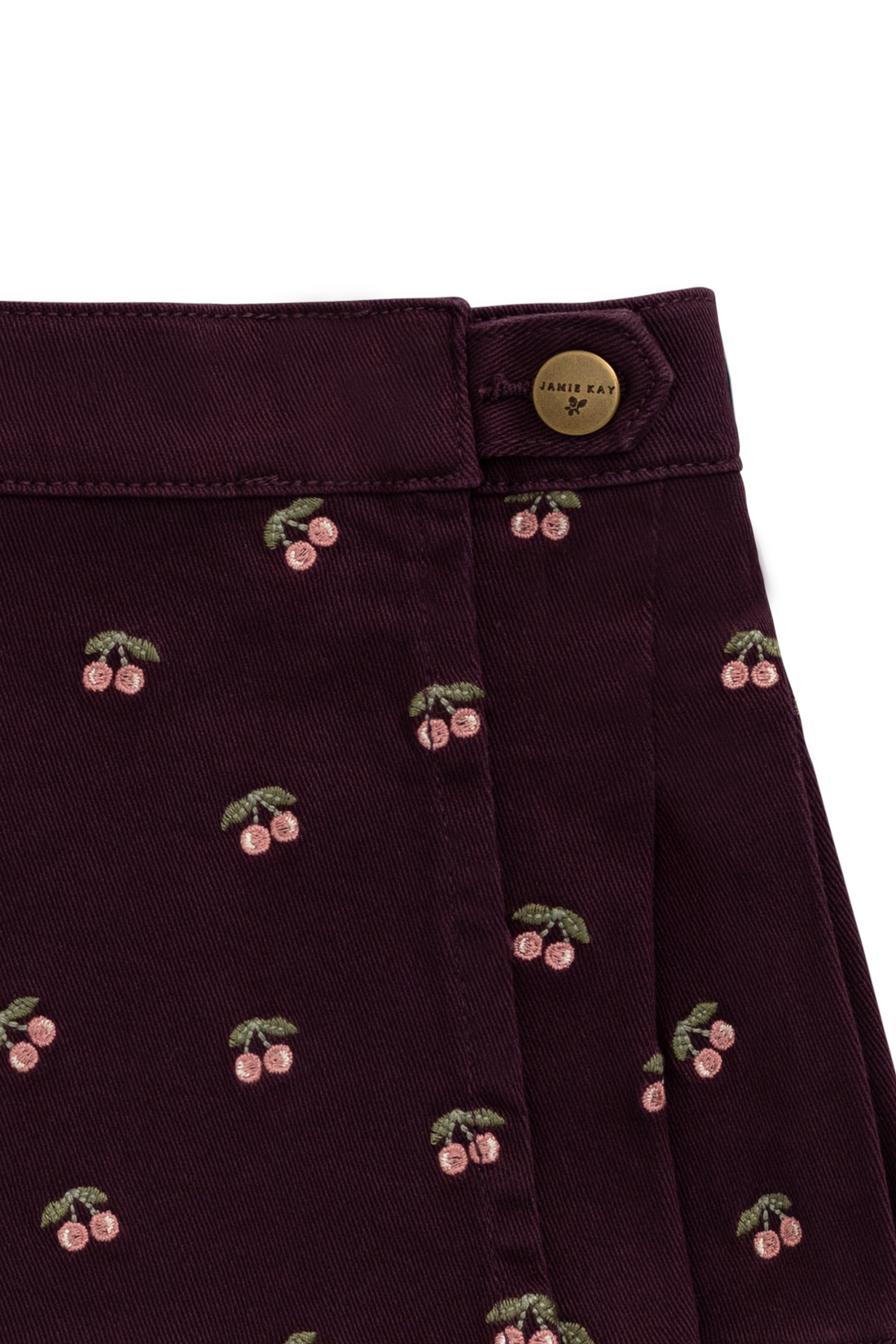 Close-up of a dark plum purple skirt featuring an embroidered cherry pattern and a gold button closure.