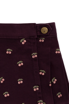 Close-up of a dark plum purple skirt featuring an embroidered cherry pattern and a gold button closure.