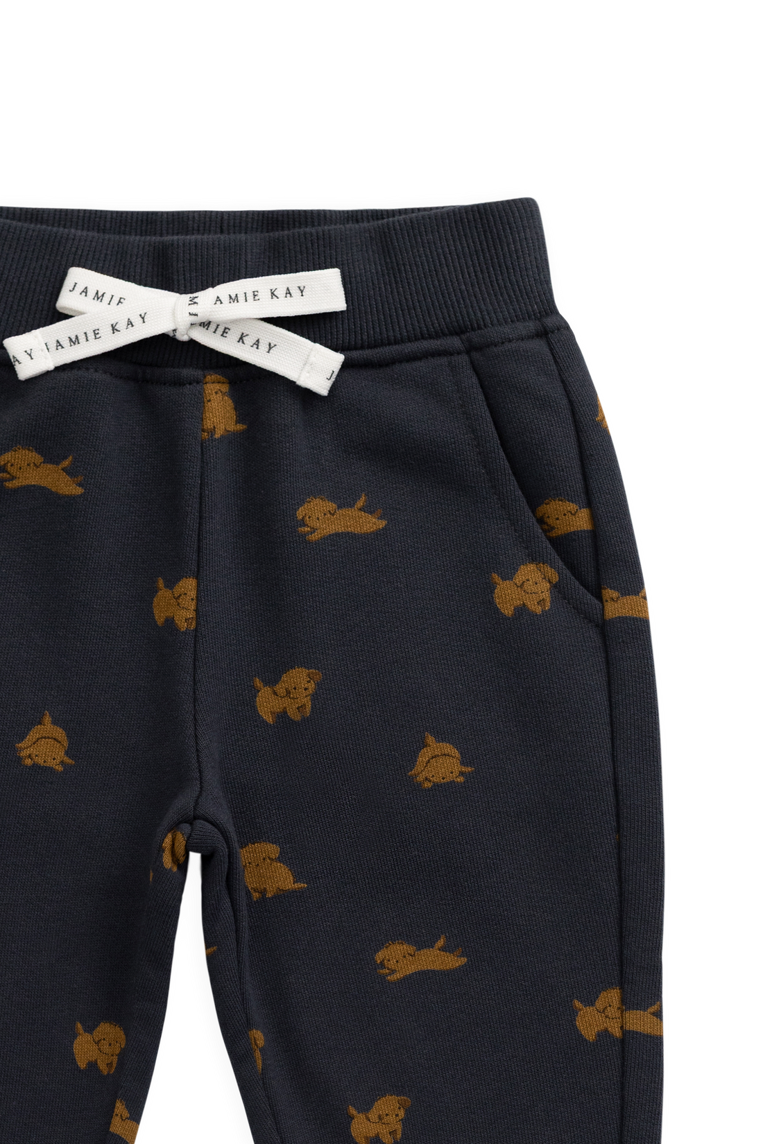 Close-up of a pair of dark navy pants with a repeating tan dog print, featuring a white drawstring bow with the brand name 'Jamie's Kay' printed on it.