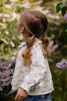 Child with braided hair standing in a garden with blurred flowers in the background