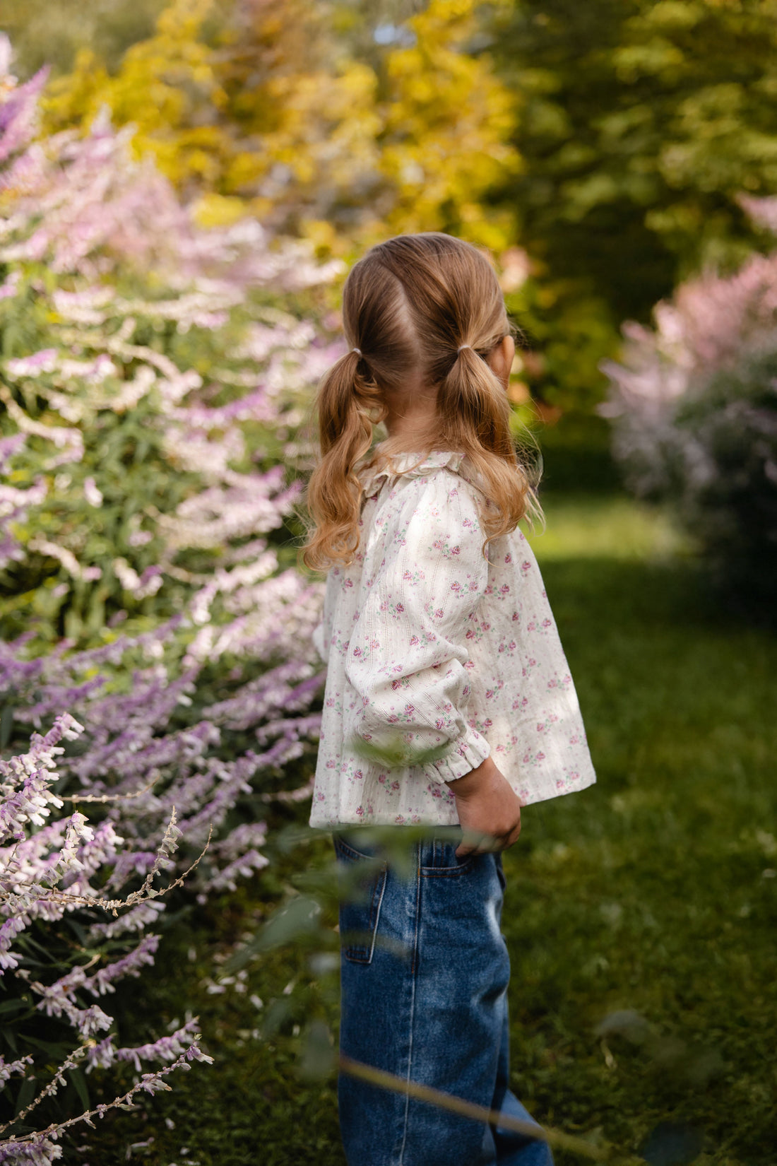 Young girl standing in a garden with flowers and trees in the background