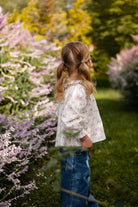 Young girl standing in a garden with flowers and trees in the background