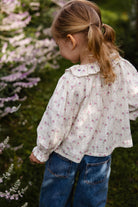 Child wearing a floral blouse and blue jeans standing in a garden with flowers.
