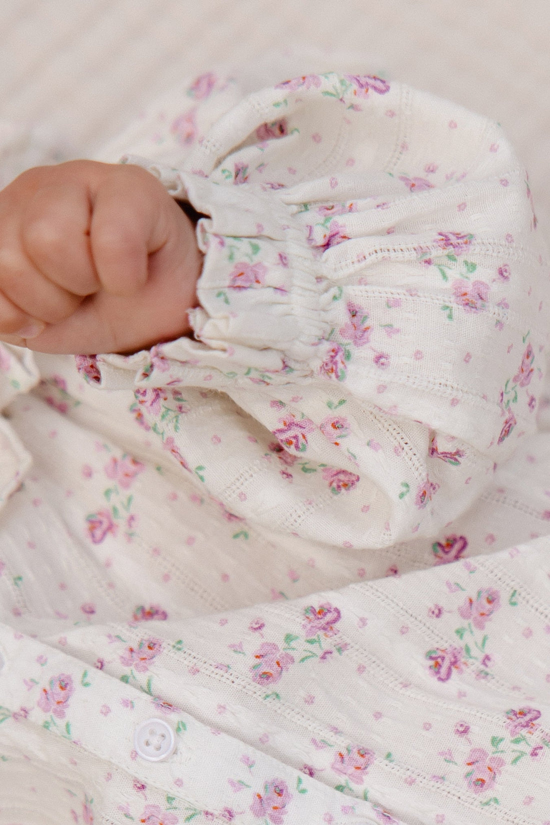 Close-up of a baby's hand holding a floral-patterned fabric with pink flowers on a light background.