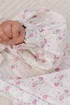 Close-up of a baby's hand holding a floral-patterned fabric with pink flowers on a light background.