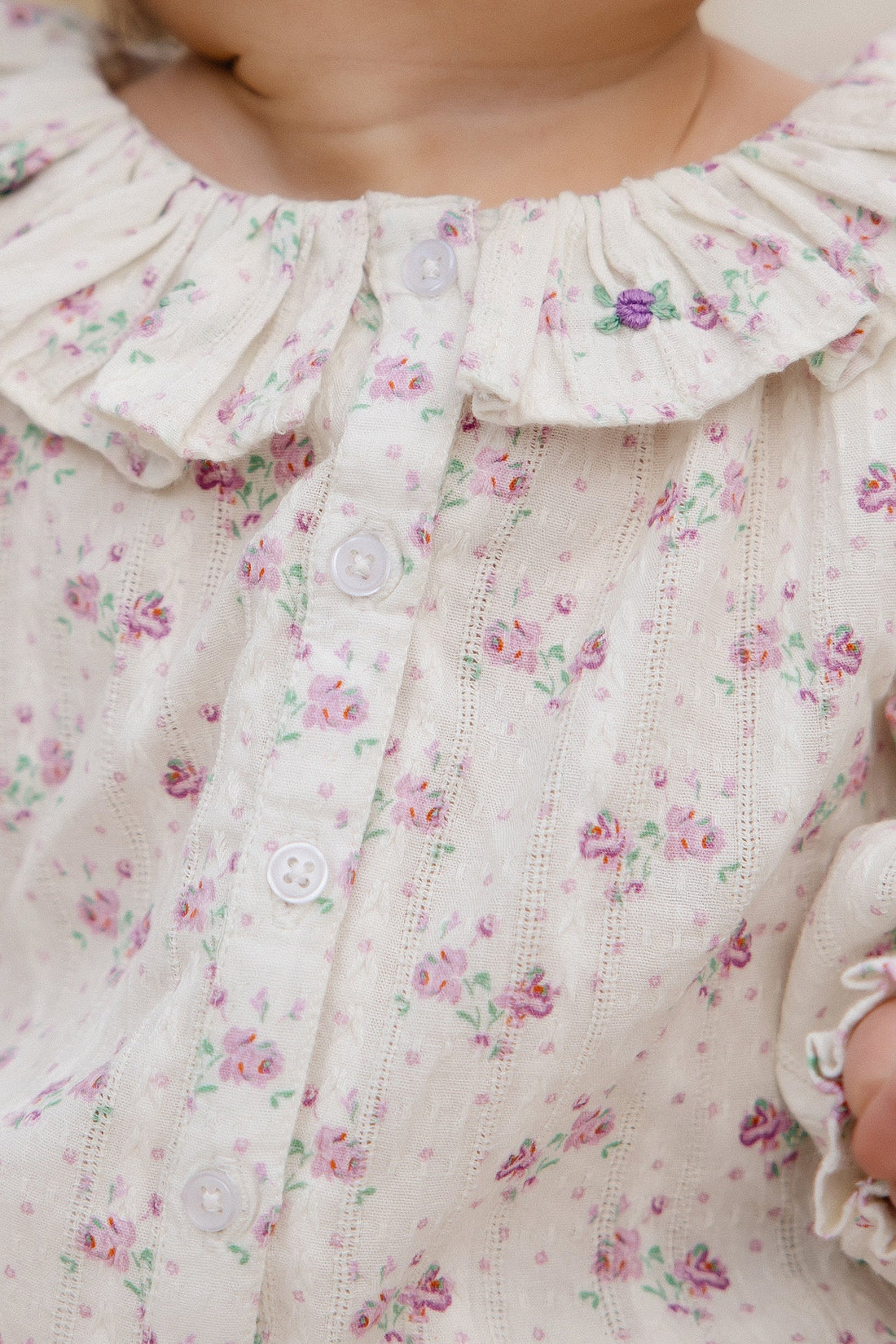 Close-up of a child's floral dress with ruffled collar and buttons.