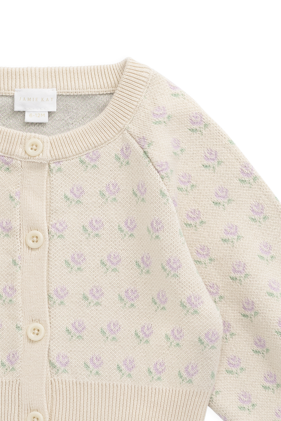 Close-up of a cream-colored knit cardigan sweater featuring a delicate all-over pattern of small purple flowers with green leaves, accented by a ribbed collar, cuffs, and hem, and a button closure.