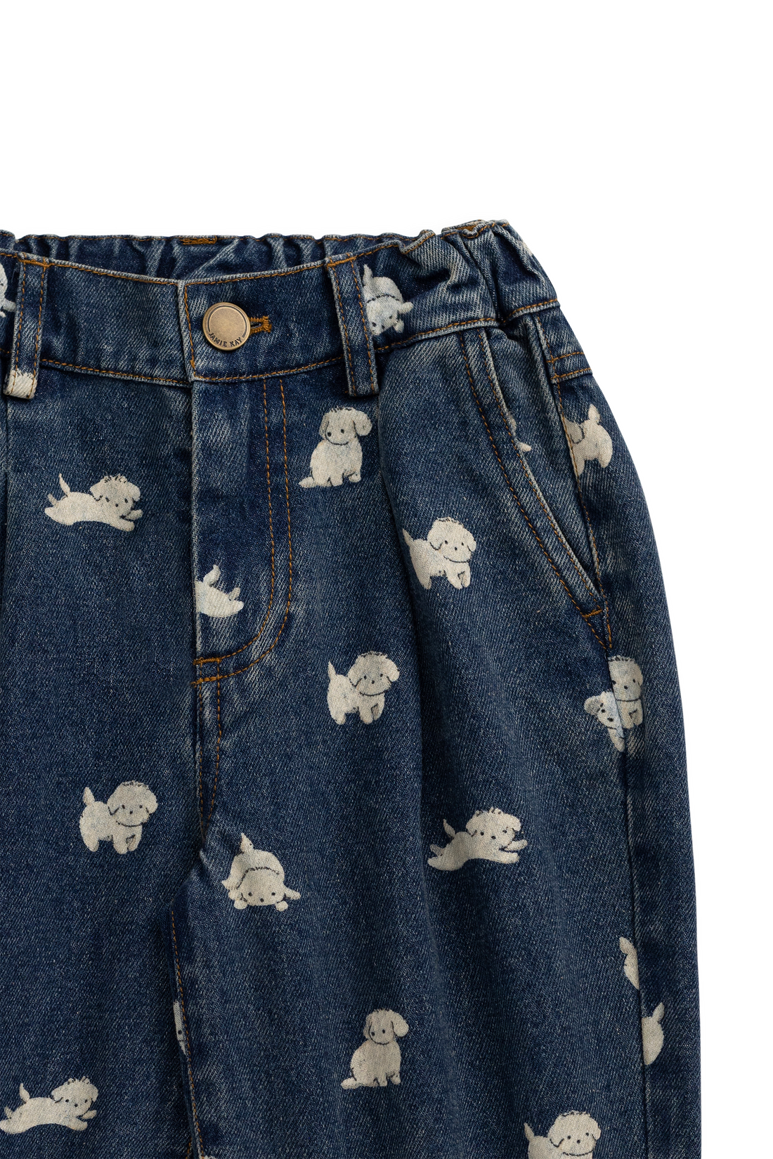 Close-up of dark blue denim pants with an allover print of small white cartoon dogs, showing the waistband, button, belt loops, and front pockets.