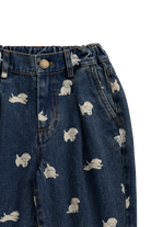 Close-up of dark blue denim pants with an allover print of small white cartoon dogs, showing the waistband, button, belt loops, and front pockets.