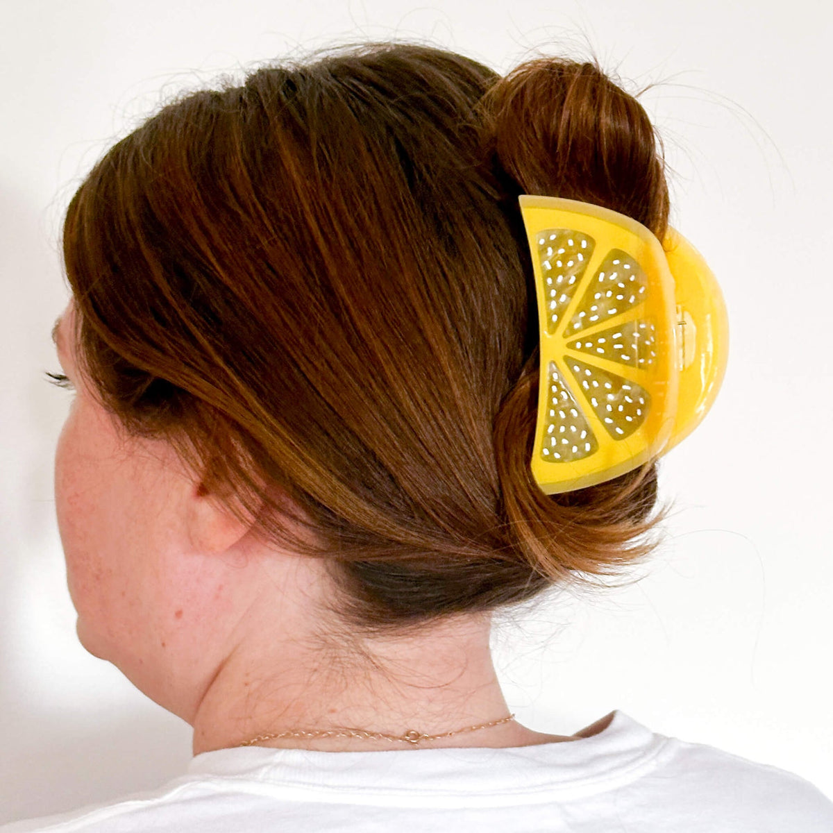 Person with a yellow lemon-shaped hair clip in their hair against a white background