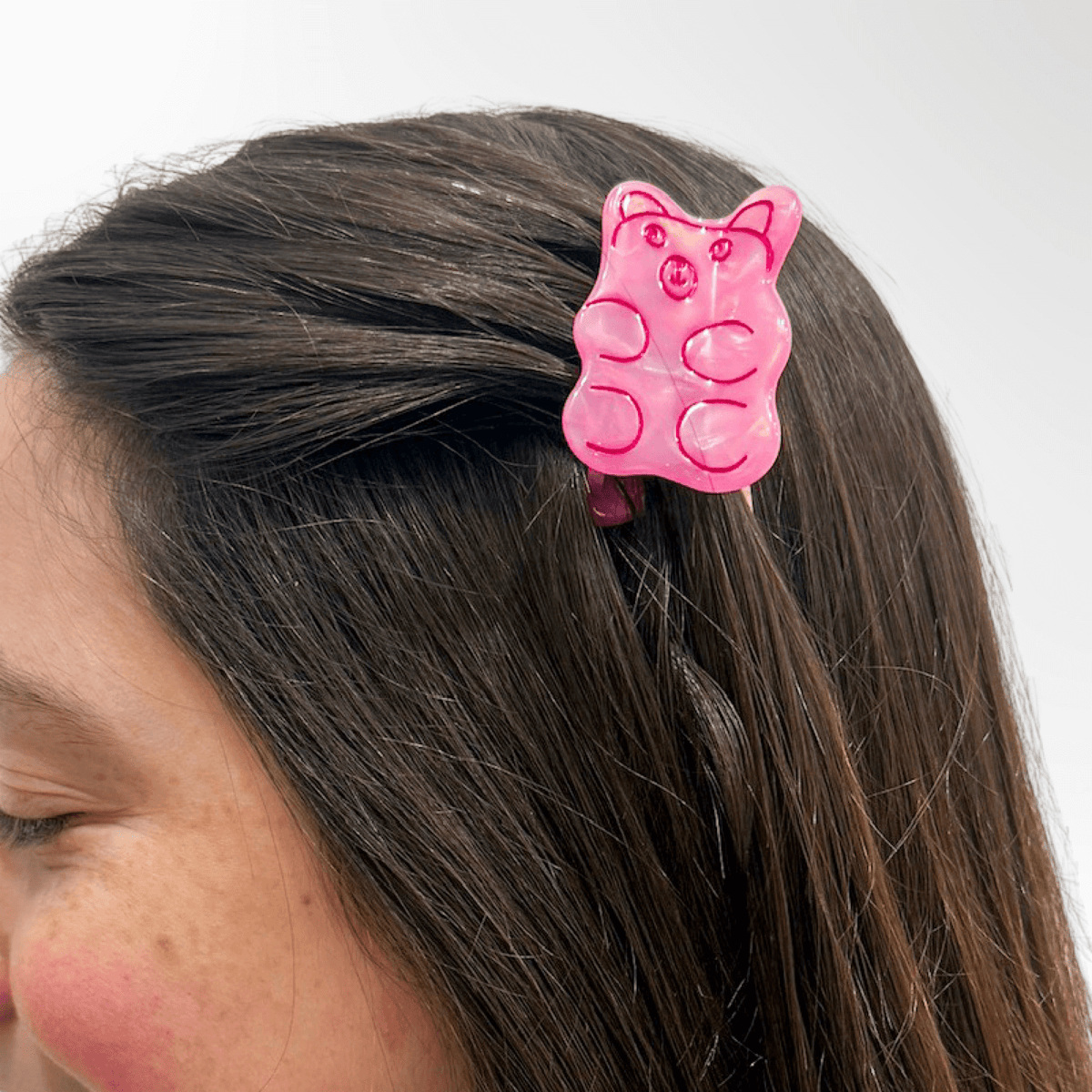 Person wearing a pink gummy bear hair clip on a white background
