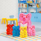 Colorful gummy bear-shaped molds on a checkered mat with a child's room in the background.