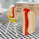 Two hot dog-shaped chairs with buns and sausages on a checkered floor in a kitchen setting.
