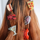 Hair accessories shaped like a hot dog, pizza slice, lobster, and other items on a person's hair.