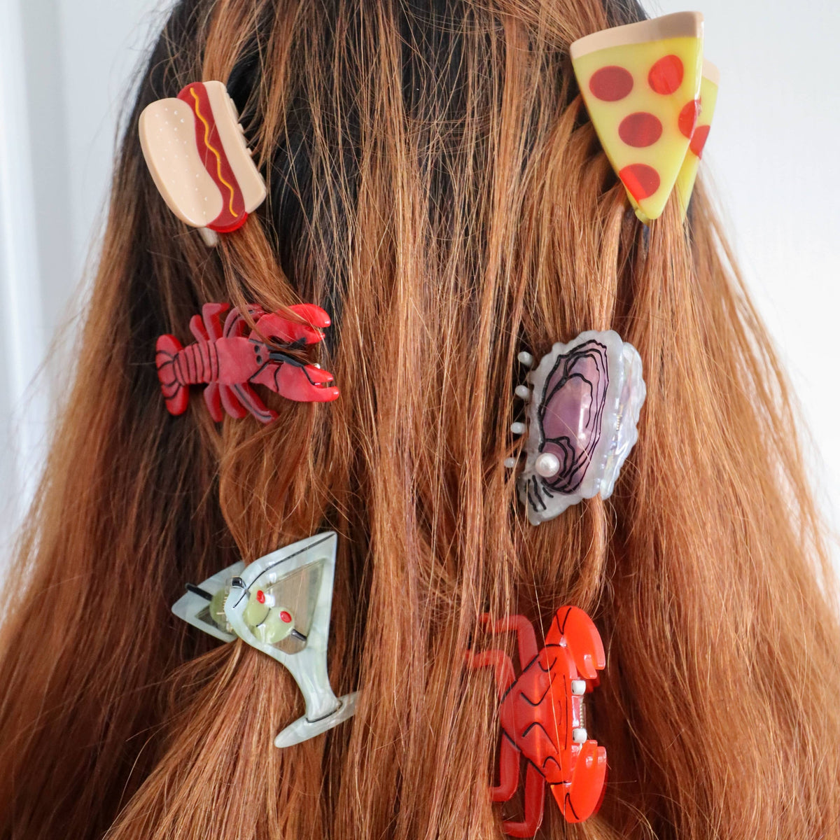 Hair accessories shaped like a hot dog, pizza slice, lobster, and other items on a person's hair.