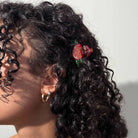 Close-up of a person with curly hair wearing a decorative hair clip against a neutral background