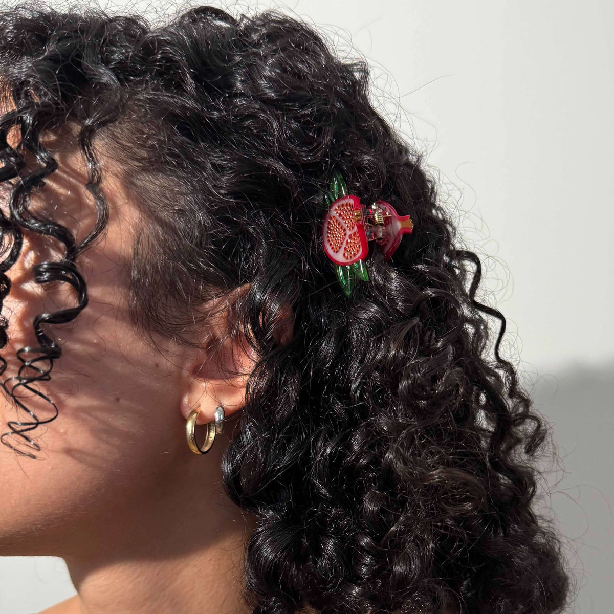 Close-up of a person with curly hair wearing a decorative hair clip against a neutral background