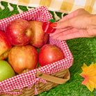 Basket of apples with a hand holding a cherry on a checkered cloth background