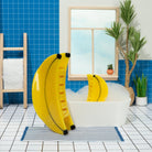 Yellow inflatable ring with banana design on a bathtub in a bathroom with blue tiles and plants.