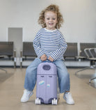Child sitting on a purple suitcase in an airport waiting area