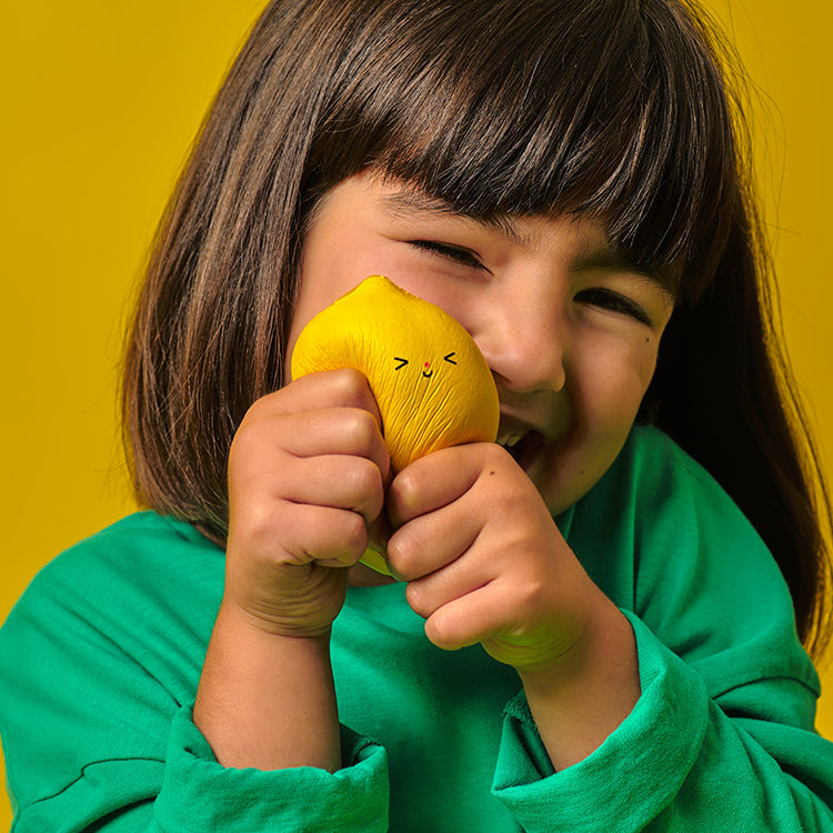 Child holding a yellow plush toy with a smiley face against a yellow background