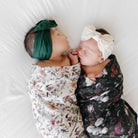 Two babies wrapped in floral swaddles with headbands on a white background