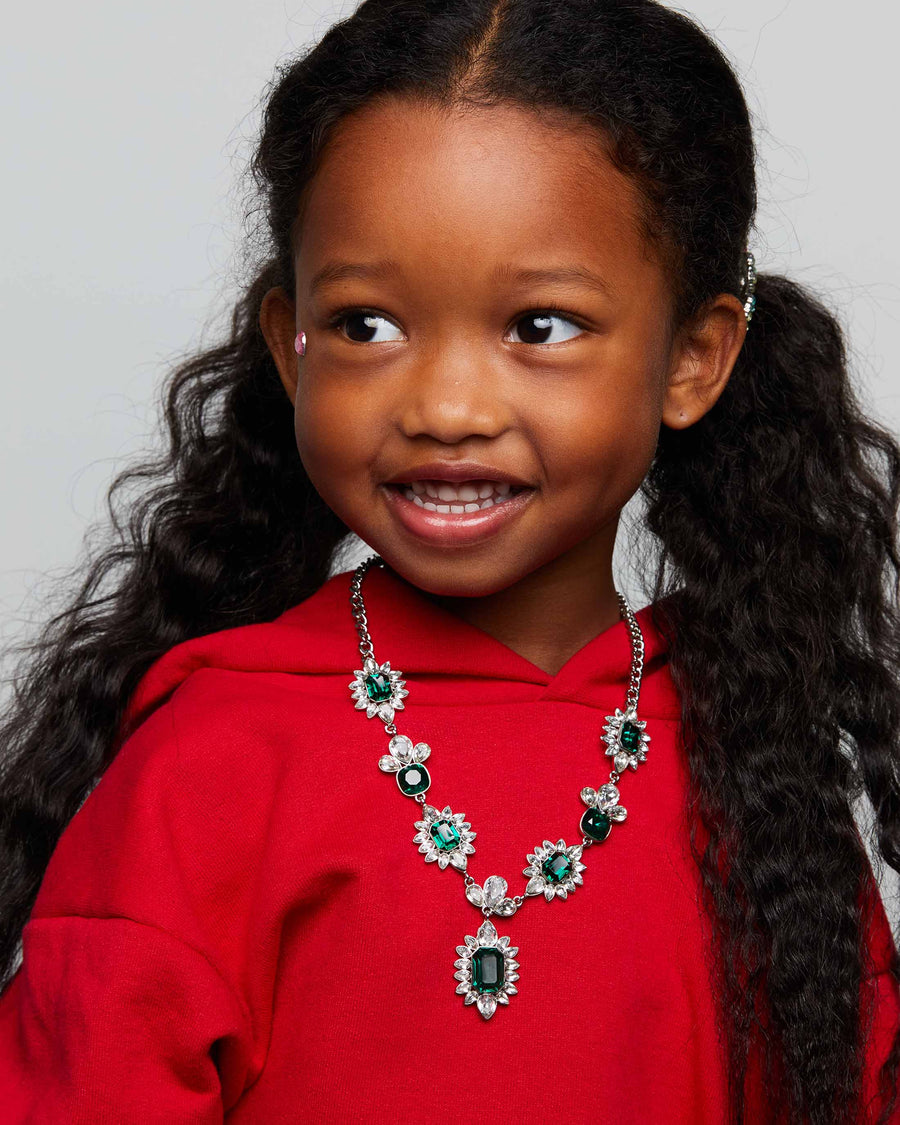 Young girl wearing a red hoodie and a decorative necklace with green and silver elements.