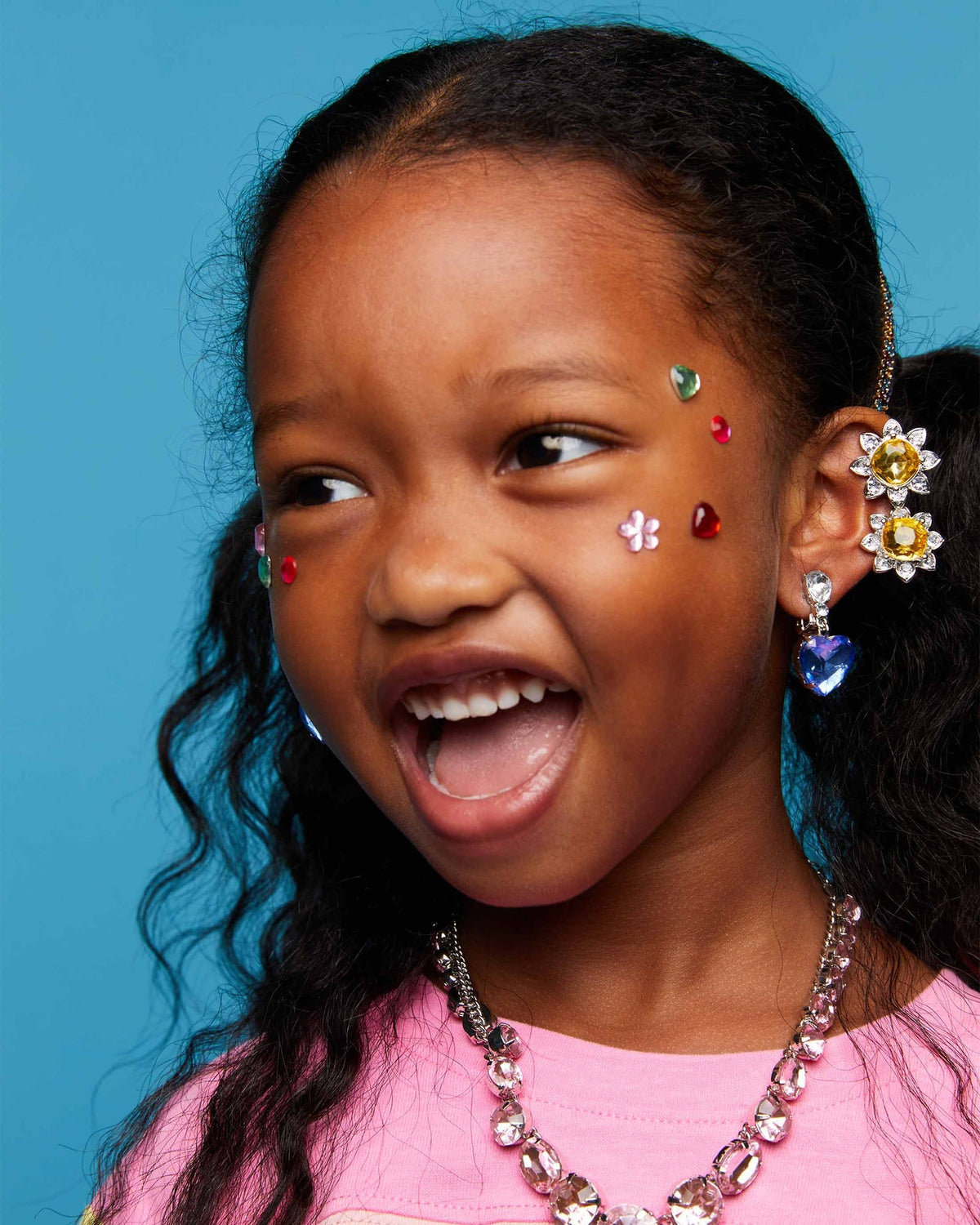 Child wearing colorful earrings and jewelry against a blue background