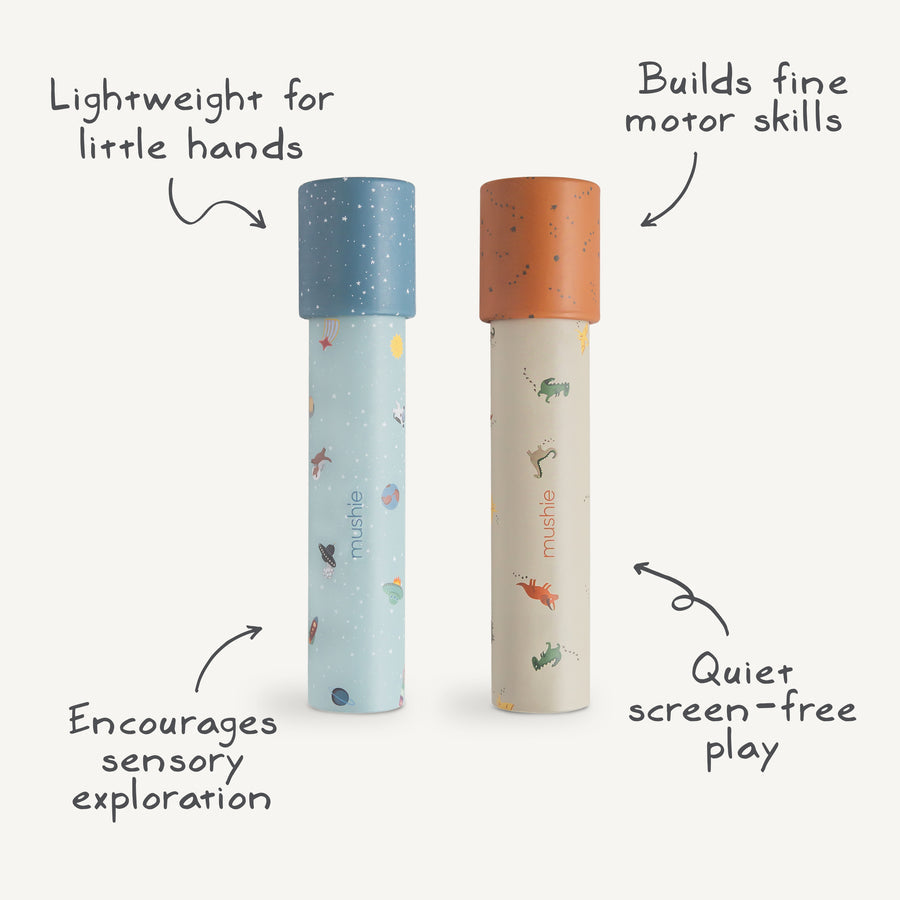 Two Mushie paper kaleidoscopes standing vertically against a white background, featuring the Space and Dinosaurs pattern, surrounded by handwritten text highlights reading "Lightweight for little hands", "Builds fine motor skills", "Encourages sensory exploration", and "Quiet screen-free play".