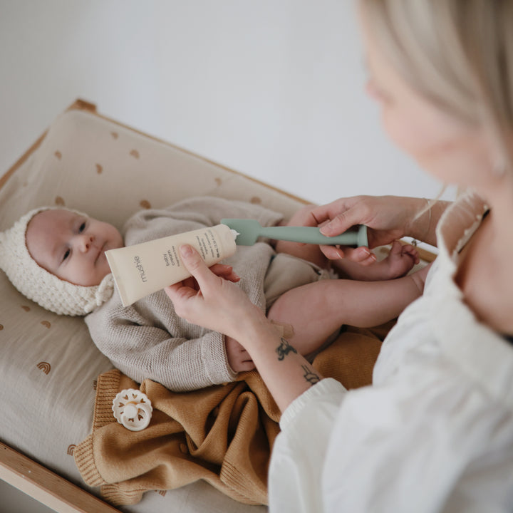 Baby lying in a crib with a woman applying lotion to the baby's skin.