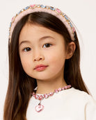Young girl wearing a pink headband and necklace with a white background