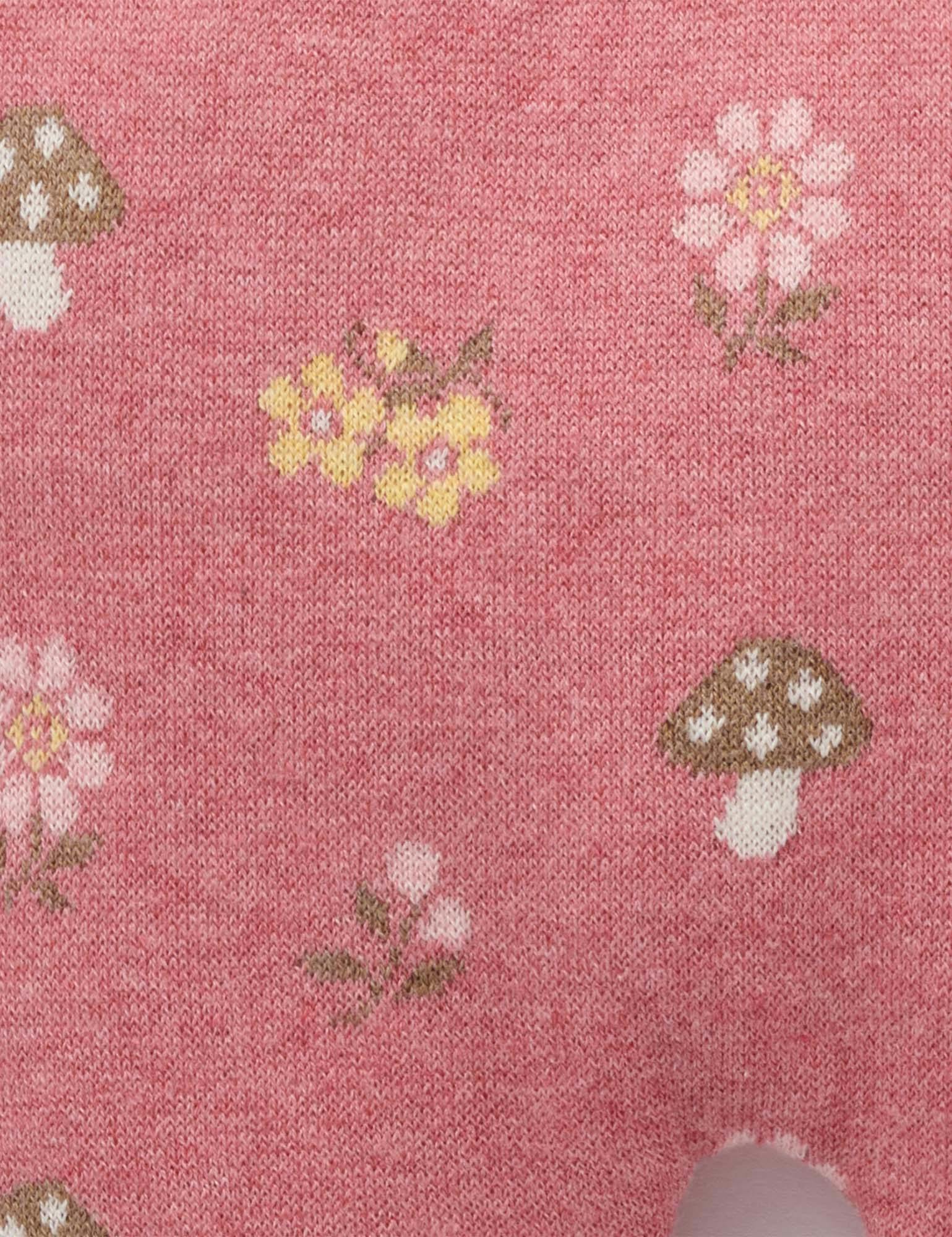 A close-up of a pink knit fabric with a repeating pattern of small yellow flowers, pink daisies, and brown-and-white mushrooms.