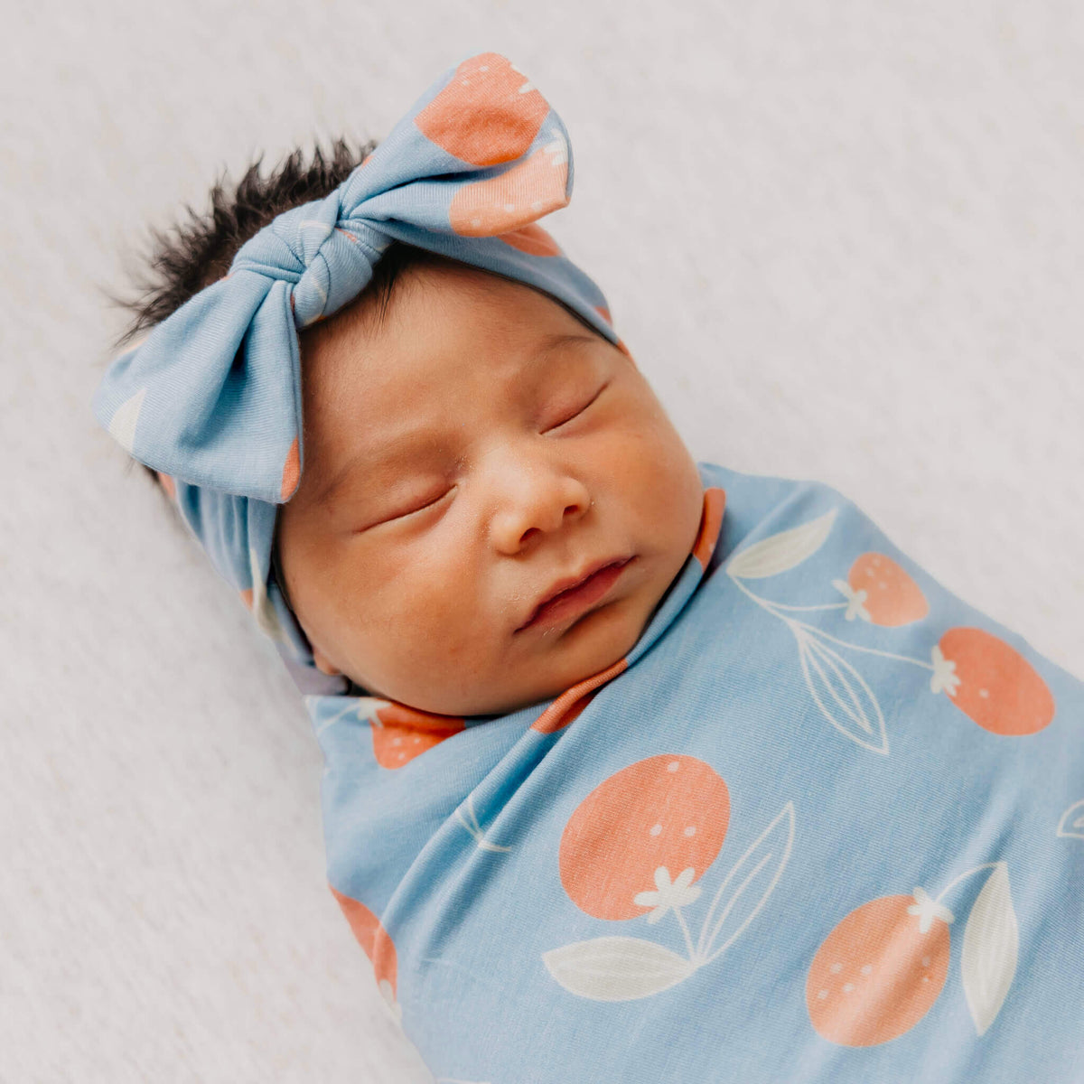 Newborn baby swaddled in a blue blanket with orange and white patterns, wearing a matching headband.