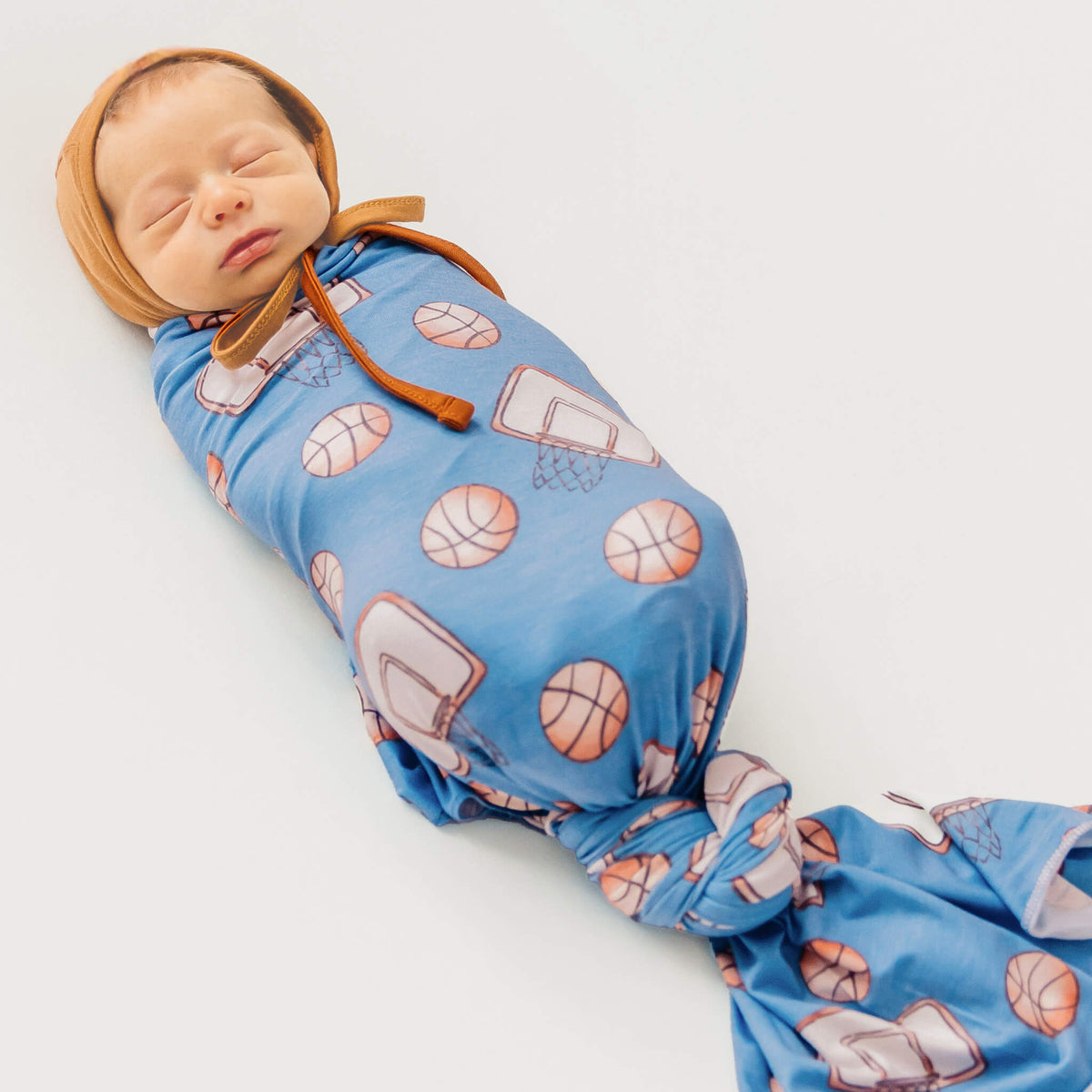 Newborn baby swaddled in a blue blanket with basketball patterns on a white background