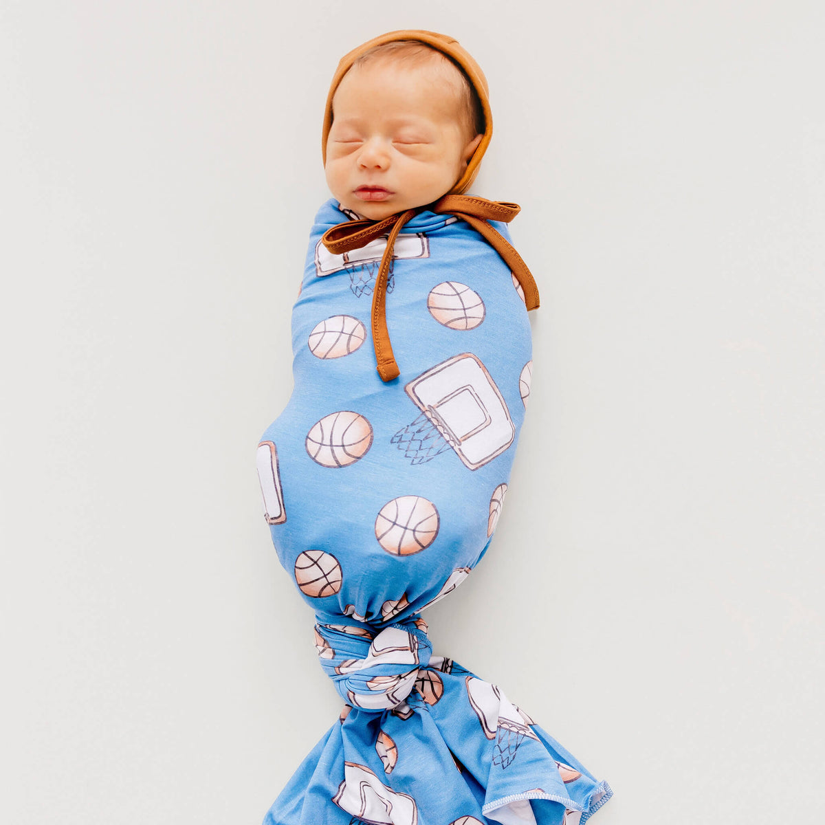 Newborn baby wrapped in a blue blanket with sports-themed patterns on a light gray background