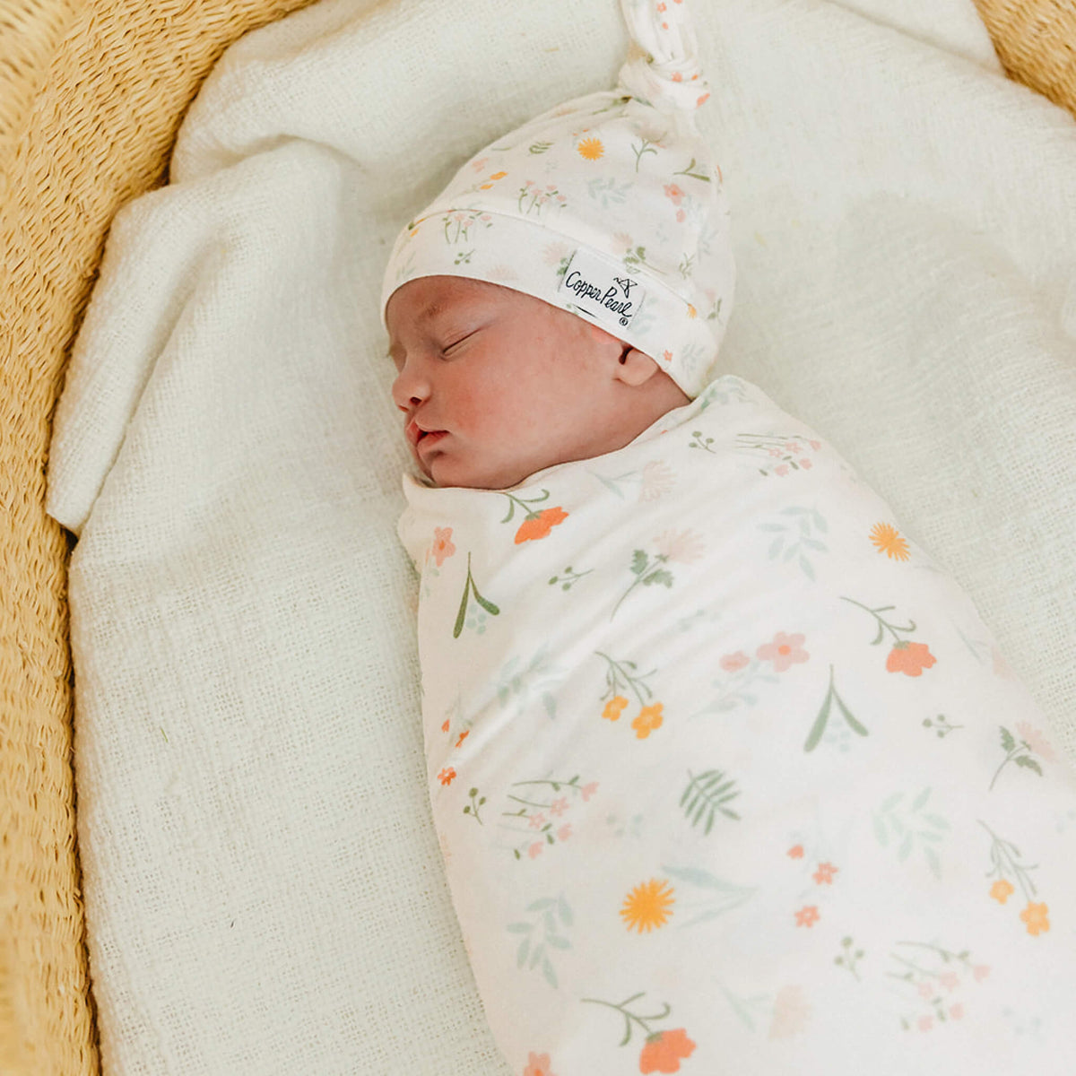 Newborn baby swaddled in a floral blanket with a matching hat, lying on a soft surface.