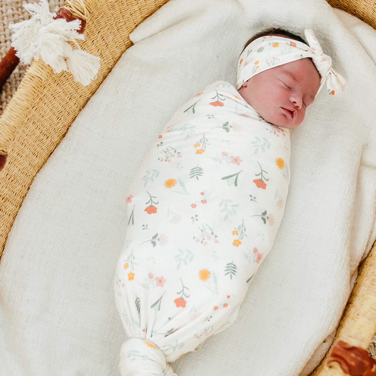 Newborn baby swaddled in a floral blanket with a headband, lying on a textured surface.