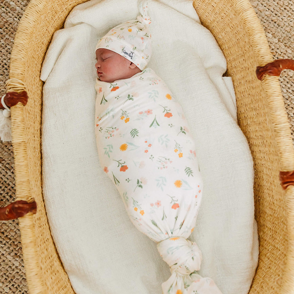 Newborn baby swaddled in a floral blanket in a moses basket.
