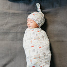 Newborn baby swaddled in a patterned blanket with a matching hat on a textured surface
