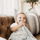 Baby holding a blanket on a couch with a neutral background