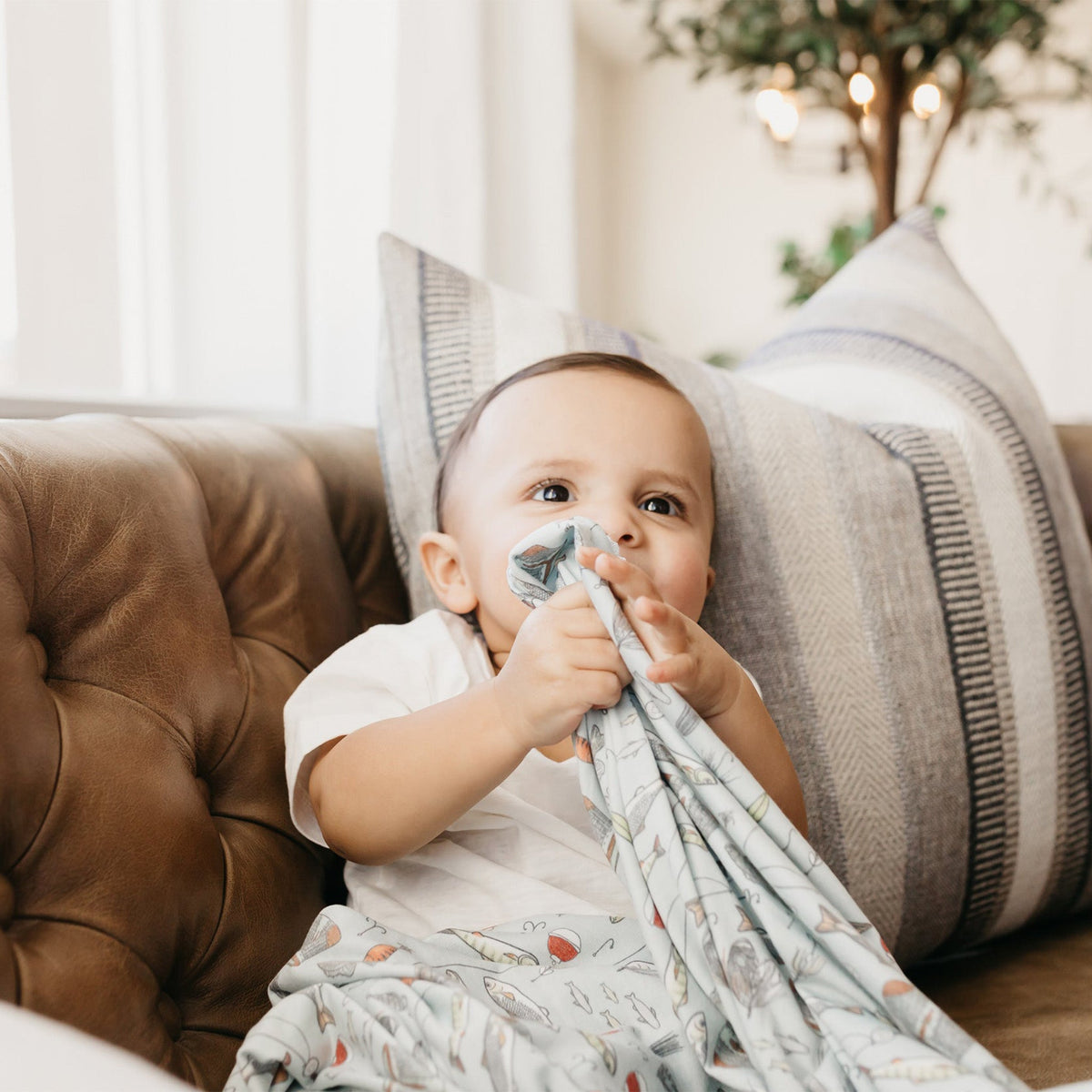 Baby holding a blanket on a couch with a neutral background
