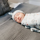 Newborn baby swaddled in a blanket with animal patterns on a textured surface.