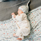 Newborn baby sleeping in a crib with a patterned blanket and hat.