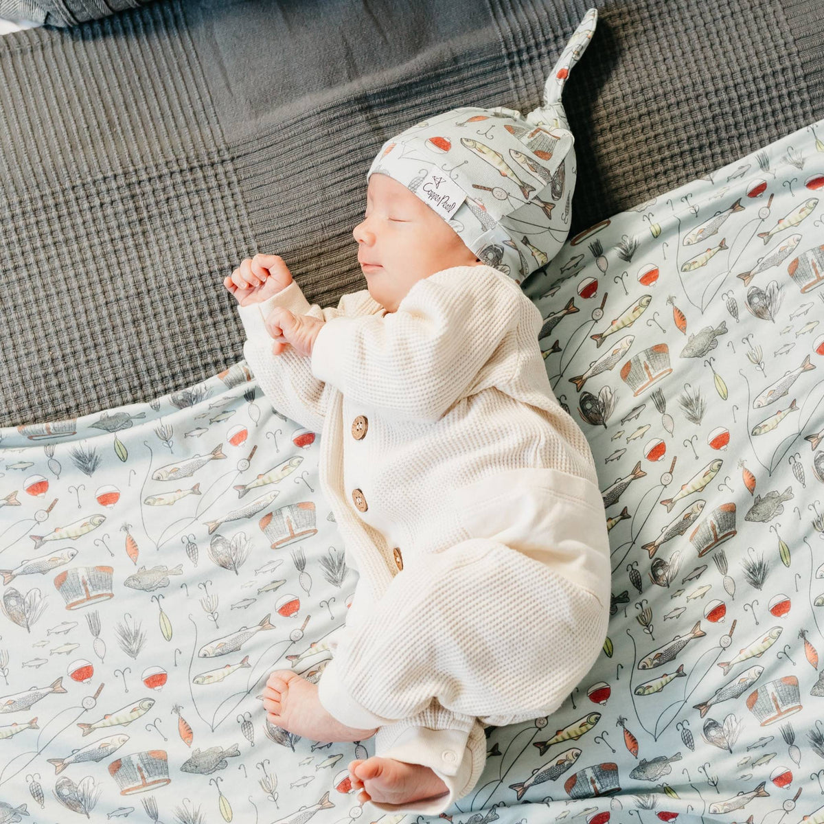 Newborn baby sleeping in a crib with a patterned blanket and hat.