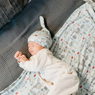 Newborn baby sleeping on a couch with a patterned blanket and hat.