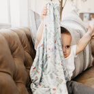 Baby holding a patterned blanket in a cozy living room setting
