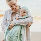 Woman holding a baby wrapped in a green blanket with a blurred background