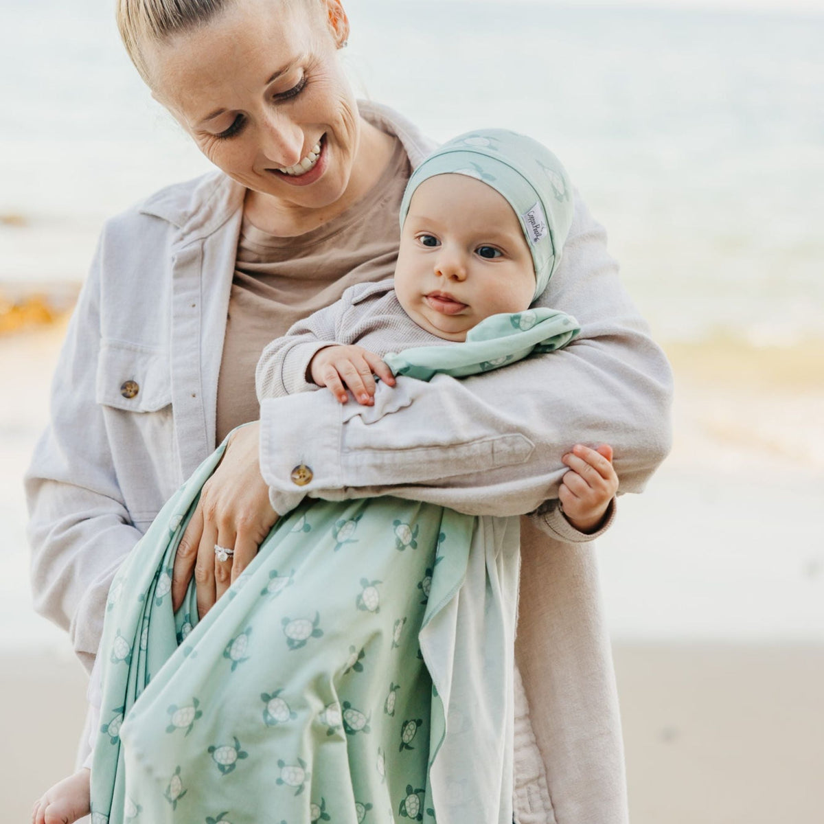Woman holding a baby wrapped in a green blanket with a blurred background