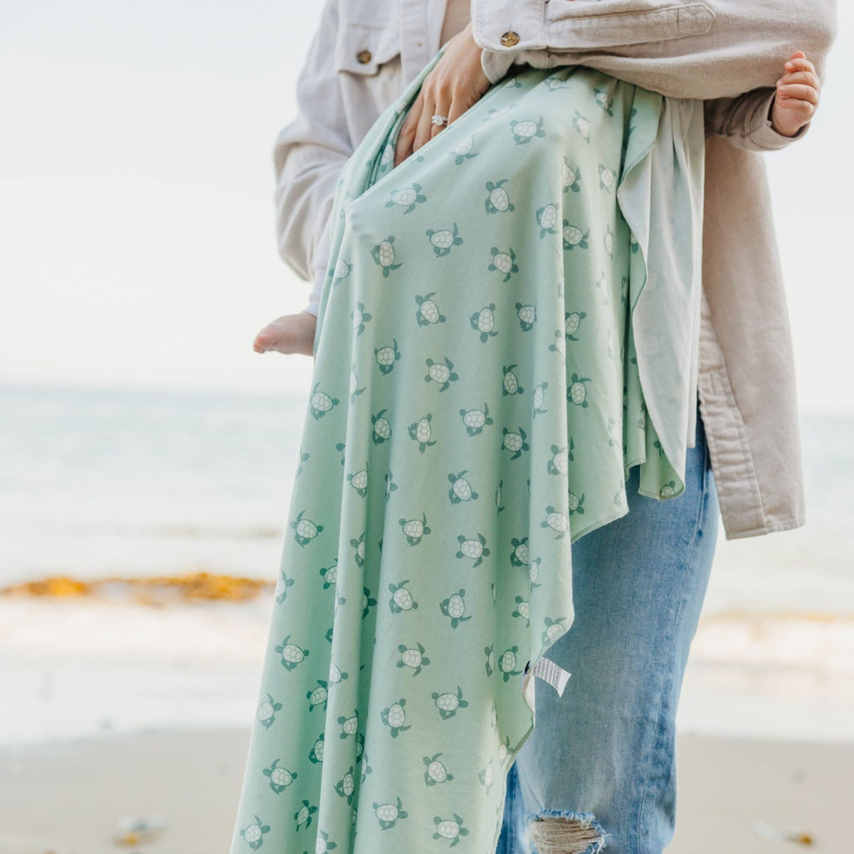 Person wearing a light green skirt with a turtle pattern on a beach.